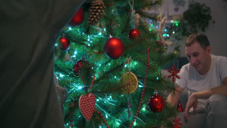 Una-Familia-Con-Dos-Niños-Decoran-Un-árbol-De-Navidad-En-Vísperas-De-Navidad.-Padre-Y-Madre-Con-Hijos-Se-Preparan-Para-El-Año-Nuevo-Y-La-Decoración-Navideña-De-La-Casa.-Imágenes-4k-De-Alta-Calidad