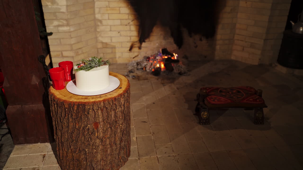 Comfortable interior in winter house. Mugs and festive cake on the background of fireplace. Cozy New Year mood.