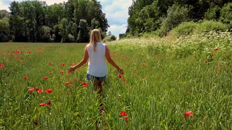 young blonde woman is walking through a poppies field feeling happy