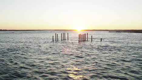 Remnants-of-building-support-poles-left-in-open-ocean-at-sunset-off-coast-of-Chincoteague-Island-Virginia,-slow-motion