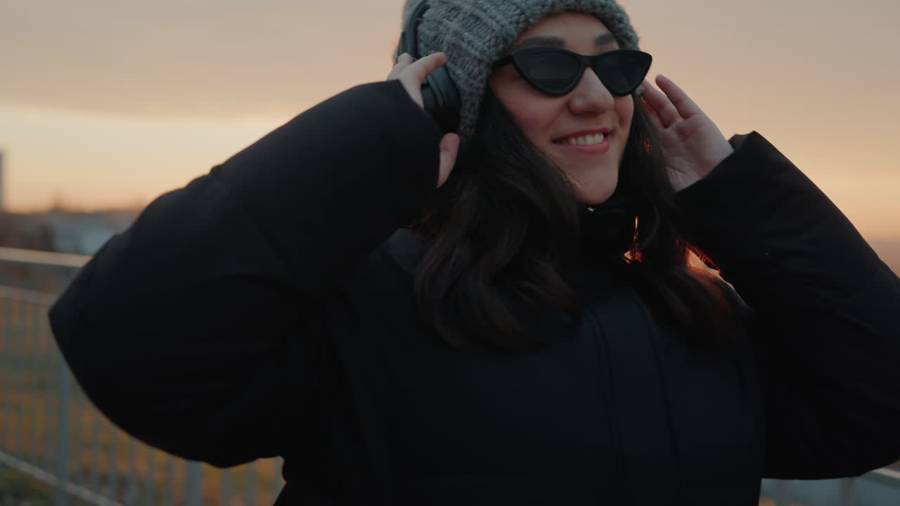 Donna che balla con gioia. Donna di città che si gode il tramonto. Donna rilassata in cappotto che balla sotto il tramonto cittadino. Un filmato spontaneo riprende una donna in abiti caldi che balla gioiosamente durante il tramonto serale.