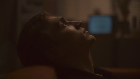 young man resting on sofa and gazing upward pensively in dimly lit room