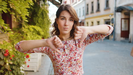 upset young woman showing thumbs down sign, disapproval, dissatisfied bad work, mistake in city