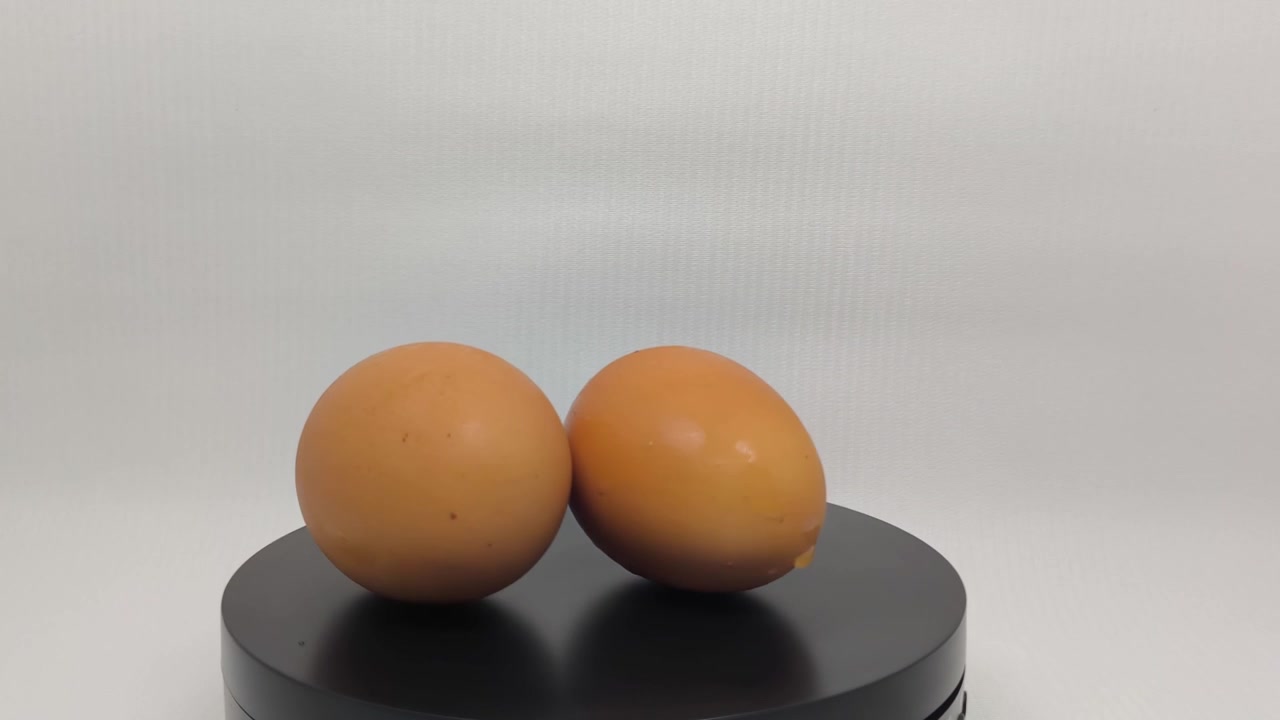 Two Brown Chicken Eggs Rotating on a Black Display Stand