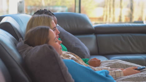 grupo de amigas adolescentes multiculturales acurrucadas bajo una manta viendo la televisión en casa