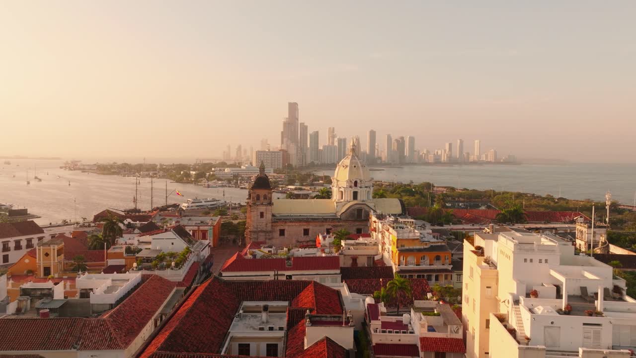 Foto aérea da torre de uma igreja no centro histórico de Cartagena ao nascer do sol, com o Santuario de San Pedro Claver e o horizonte moderno ao fundo