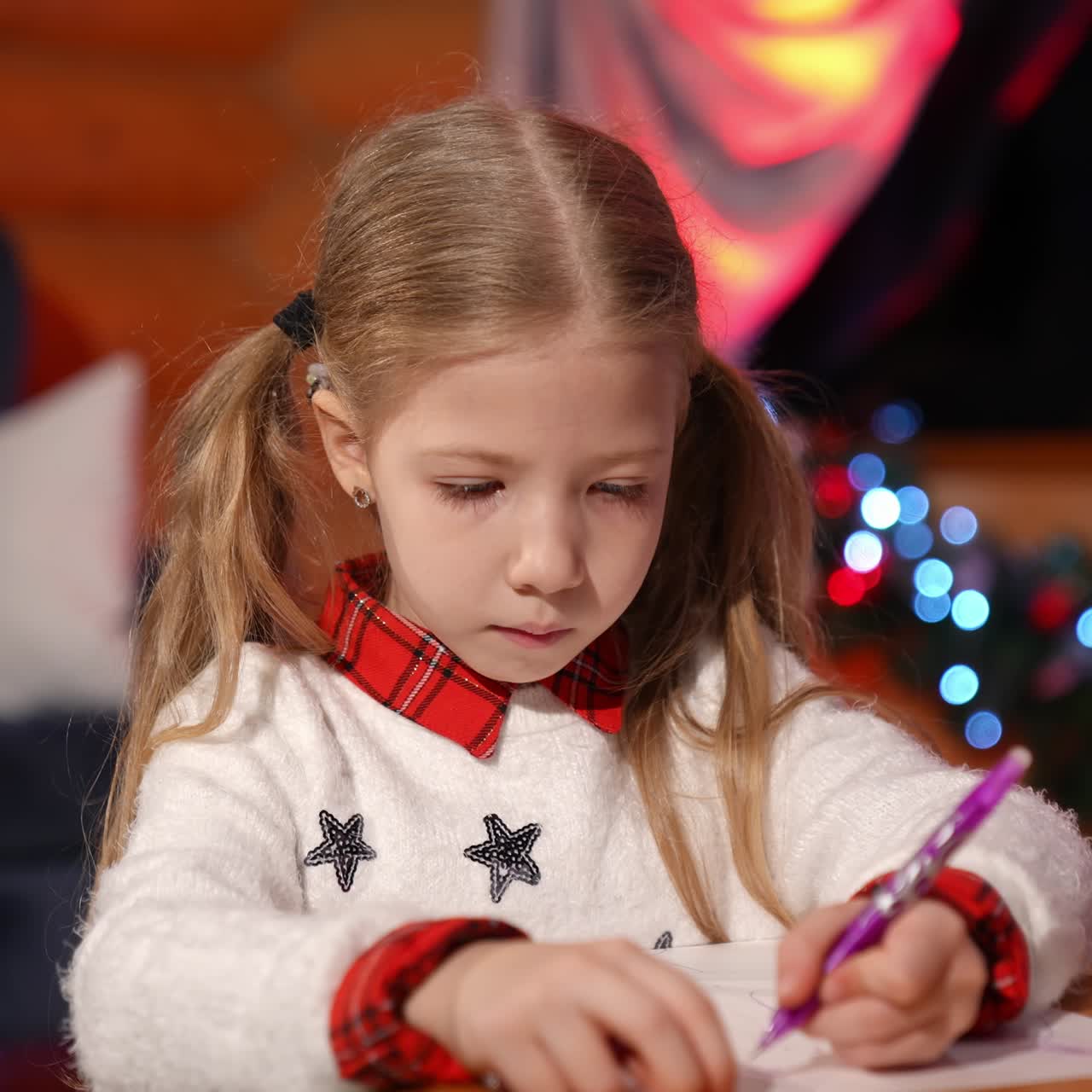 Portrait of a lovely little girl indoors at Christmas. Cute child writing a letter to Santa. Beautiful small girl drawing a picture on xmas background at home