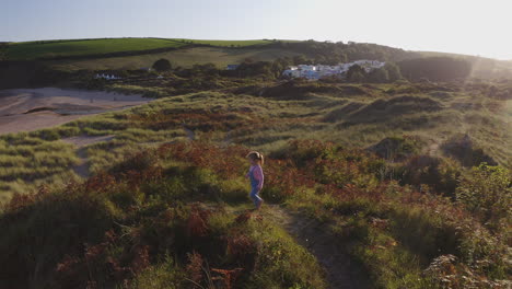 drone shot of young girl on beach vacation playing in sand dunes against flaring sun