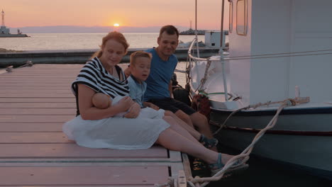 padres con el hijo mayor y el bebé sentados en el muelle al atardecer