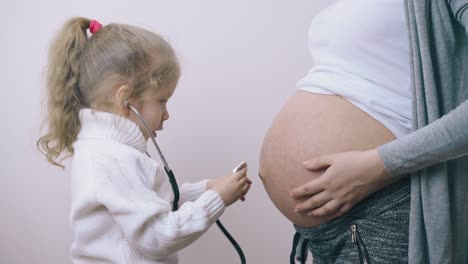 girl-puts-stethoscope-to-tummy-of-pregnant-mother-at-home