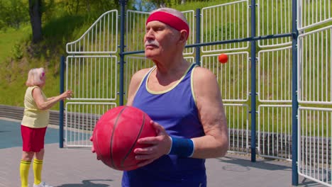 anciano abuelo posando con la pelota, mirando a la cámara al aire libre en la cancha de baloncesto