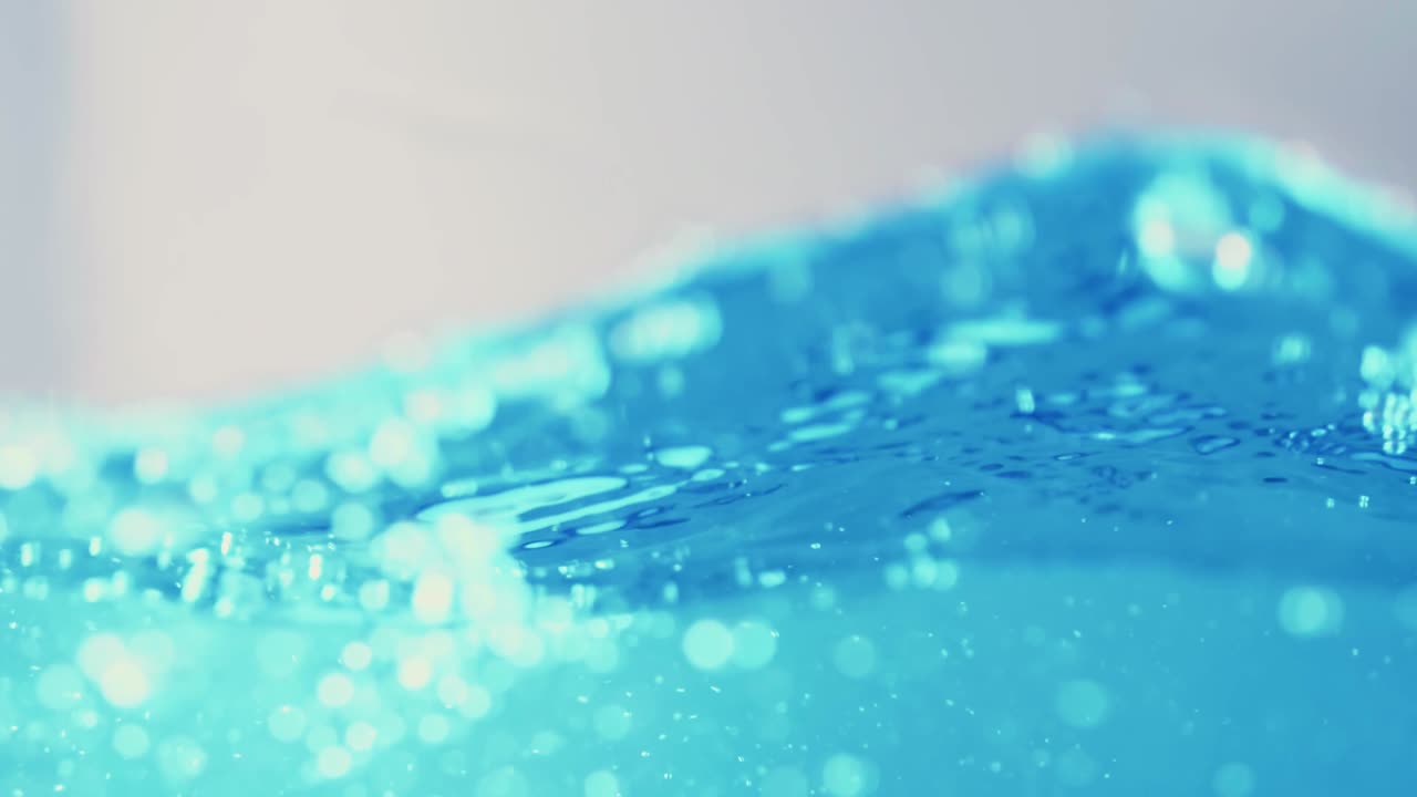 슬로우 모션의 깨끗한 물 표면은 물이 튀는 상점으로 화면을 채우고 기포로 액체 표면을 흔들고 있습니다.