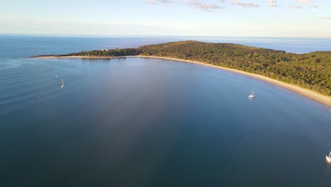 Vista-Aérea-De-La-Playa-Frente-A-La-Bahía-De-Prueba-Con-Veleros-Navegando-En-El-Mar-Azul-Al-Atardecer---Parque-Nacional-Arakoon-En-Nsw,-Australia