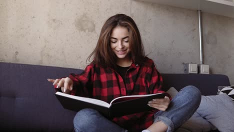joven atractiva chica morena diciendo algo y sonriendo mientras lee un libro.