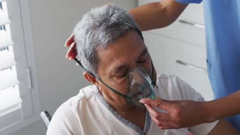 médica de raza mixta asistiendo a un anciano en cama en casa usando un ventilador