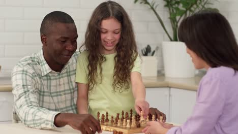 multi ethnic family of three play chess at home sitting at the table. dad and daughter win mom