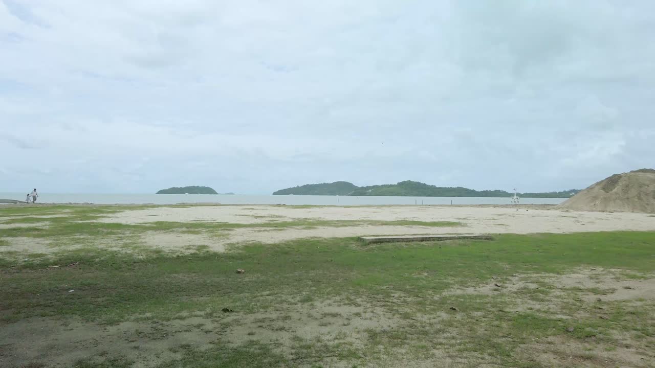 비가 오는 구름이 많은 해변에 초록색 풀이 있는 자연 모래 해변의 풍경