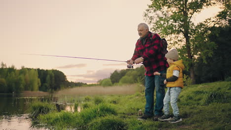 un vecchio pescatore sta mostrando a suo nipote come pescare con la canna il nonno e il bambino si stanno riposando sulla costa del lago