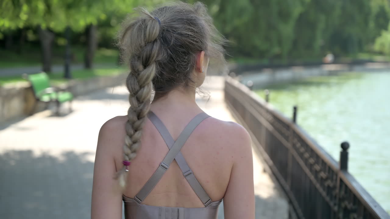 Woman in beige sportswear walking near a lake in the park