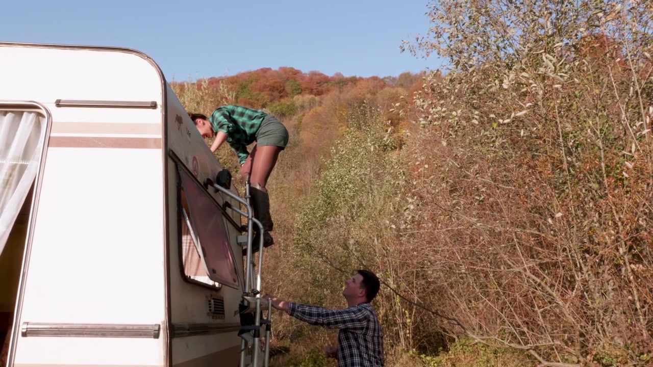Uomo aiuta la sua partner a scendere dal tetto del camper