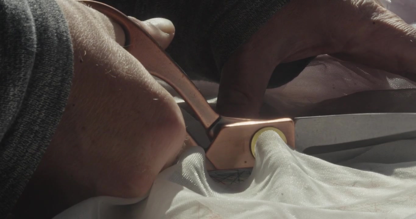 Fashion designer marking soft white veil material before carefully cutting along the line with scissors in a staged tailoring scene.