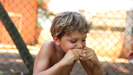 niño comiendo una naranja afuera a la luz del sol. niño joven disfrutando de una fruta saludable al aire libre en 4k
