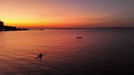 Fisherman-in-a-canoe-on-the-Paraná-River-with-the-cityscapes-of-Posadas-at-sunset-in-the-background,-Argentina