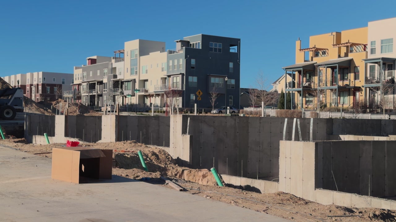 Slow left to right pan of concrete foundation forms with finished residential buildings behind.