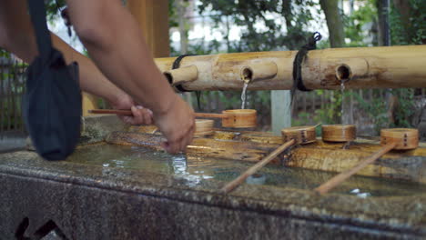 persona lavándose las manos temprano en la mañana de la manera tradicional, agua saliendo de bambú en kyoto, iluminación suave de japón