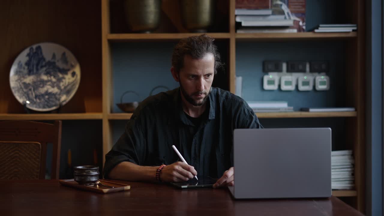 Man working on tablet with stylus and laptop at a desk