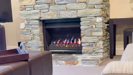 a steady shot of a gas fireplace set in a stone surround within a contemporary living room, featuring warm ambient lighting and soft furnishings