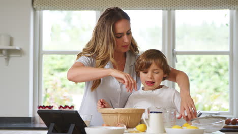 mother and son in pyjamas baking in kitchen at home following recipe on digital tablet