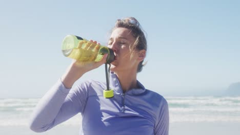 Sportliche-Frau-Trinkt-Wasser-Am-Strand