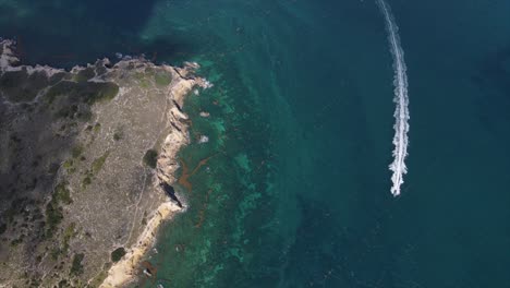 Yacht-floating-on-blue-sea-past-rocky-shore