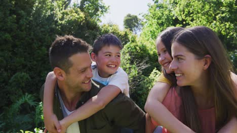 Portrait-of-caucasian-couple-carrying-son-and-daughter-on-their-back-in-the-garden