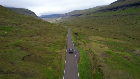 drone following a car in a one lane faroese open road with a small river on the side