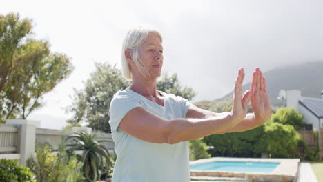 Mujer-Mayor-Caucásica-Enfocada-Practicando-Yoga-En-Un-Jardín-Soleado,-Cámara-Lenta,-Espacio-Para-Copiar