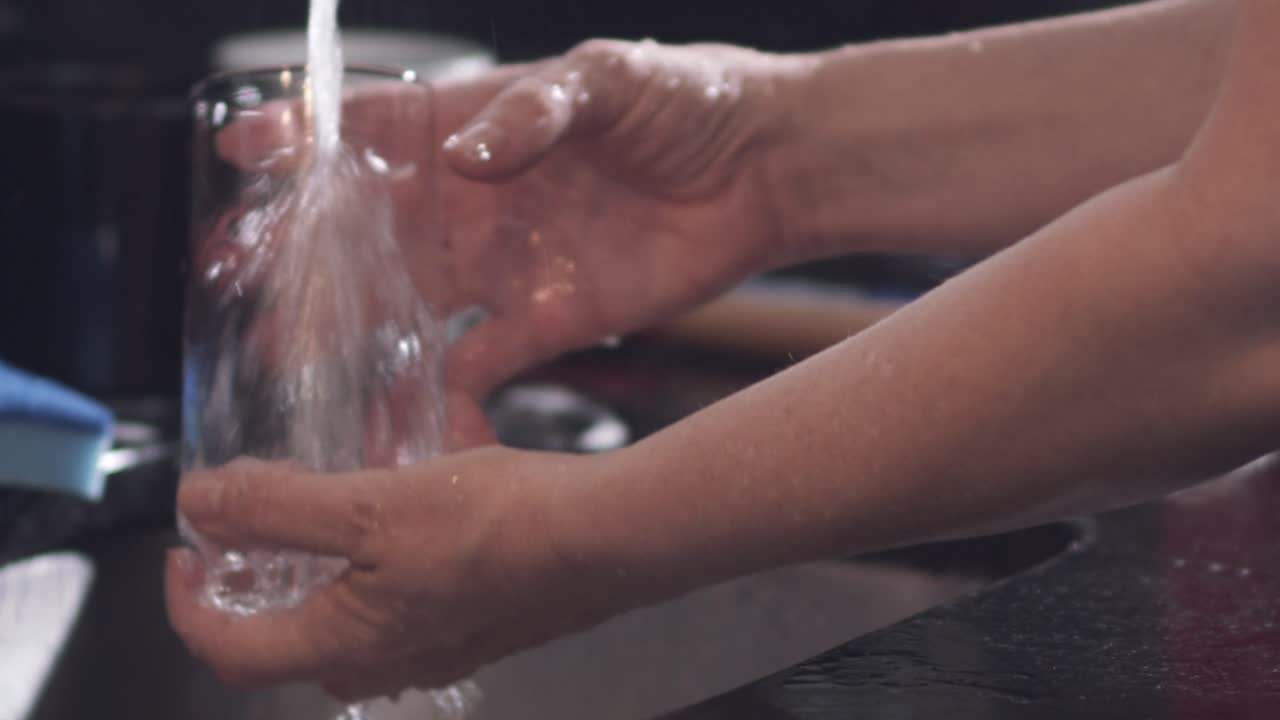 Nærbillede, husmor vasker glaskop under køkkenhane derhjemme, slowmotion