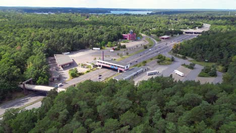 cars driving on a freeway interchange surrounded by forest leading to a lake on a cloudy day