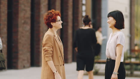 two businesswomen shaking hands and talking on street