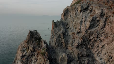 Patmos,-Griechenland,-Insel,-Drohne,-Luftaufnahme,-Mann,-Der-Auf-Einer-Klippe-Steht-Und-Auf-Den-Ozean-Blickt,-Drohnenaufnahme-Eines-Sonnenuntergangs-Aus-Der-Luft