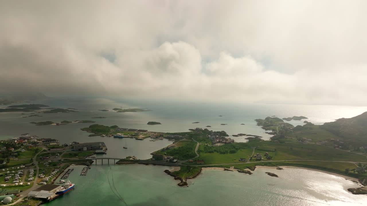 Sommarøy island, picturesque fishing village with bridge and harbor surrounded by archipelago under cloudy summer sky, Norway. Aerial forward