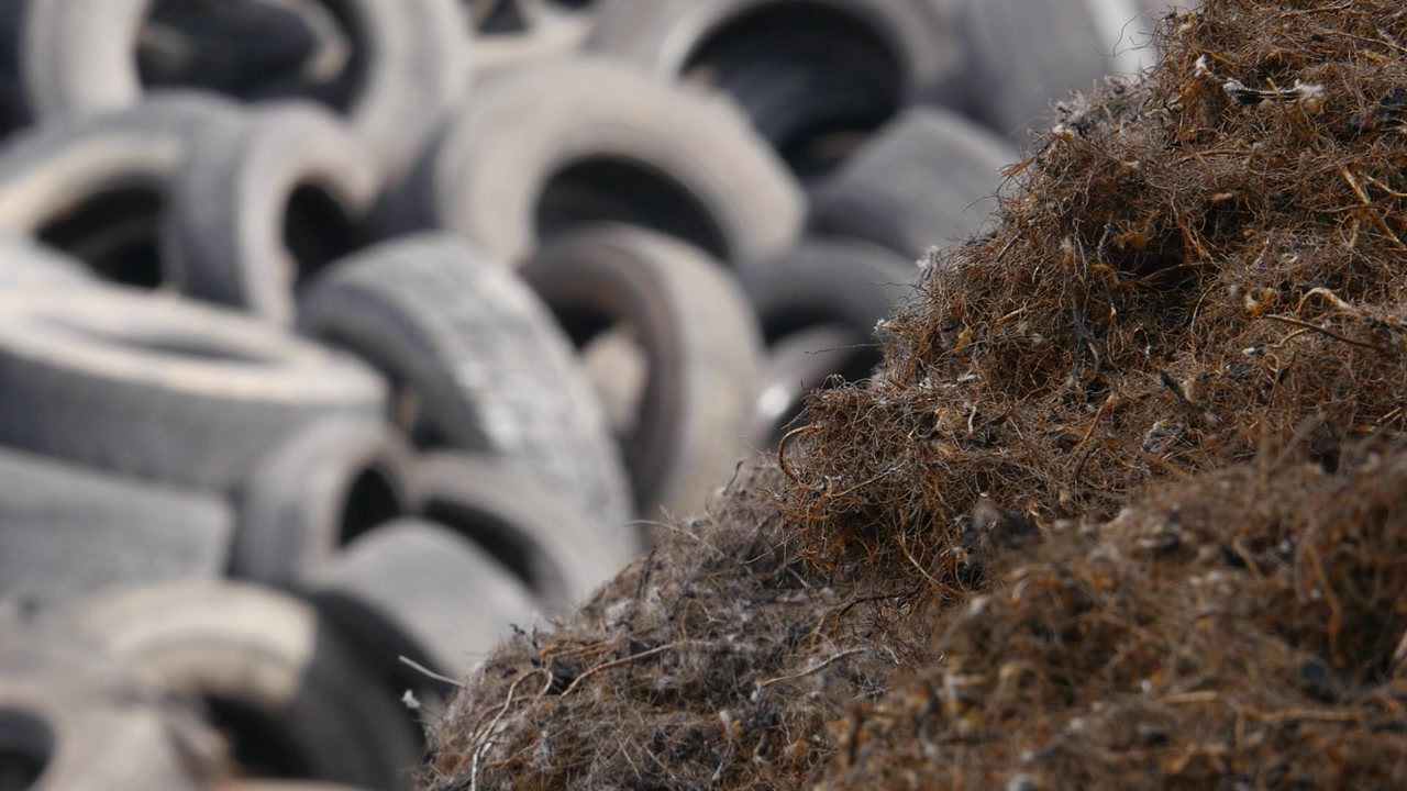 Close up shot of a pile of shredded steel wire mesh extracted from old tires during the recycling process. Used tires blurred in the background. Waste management concept.