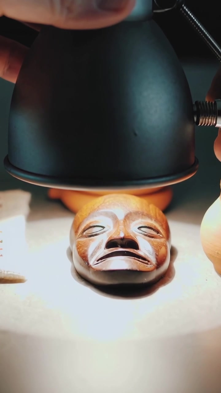 Video verticale: Una mano che entra regola e abbassa una lampada su una panca per illuminare una maschera e degli anelli.