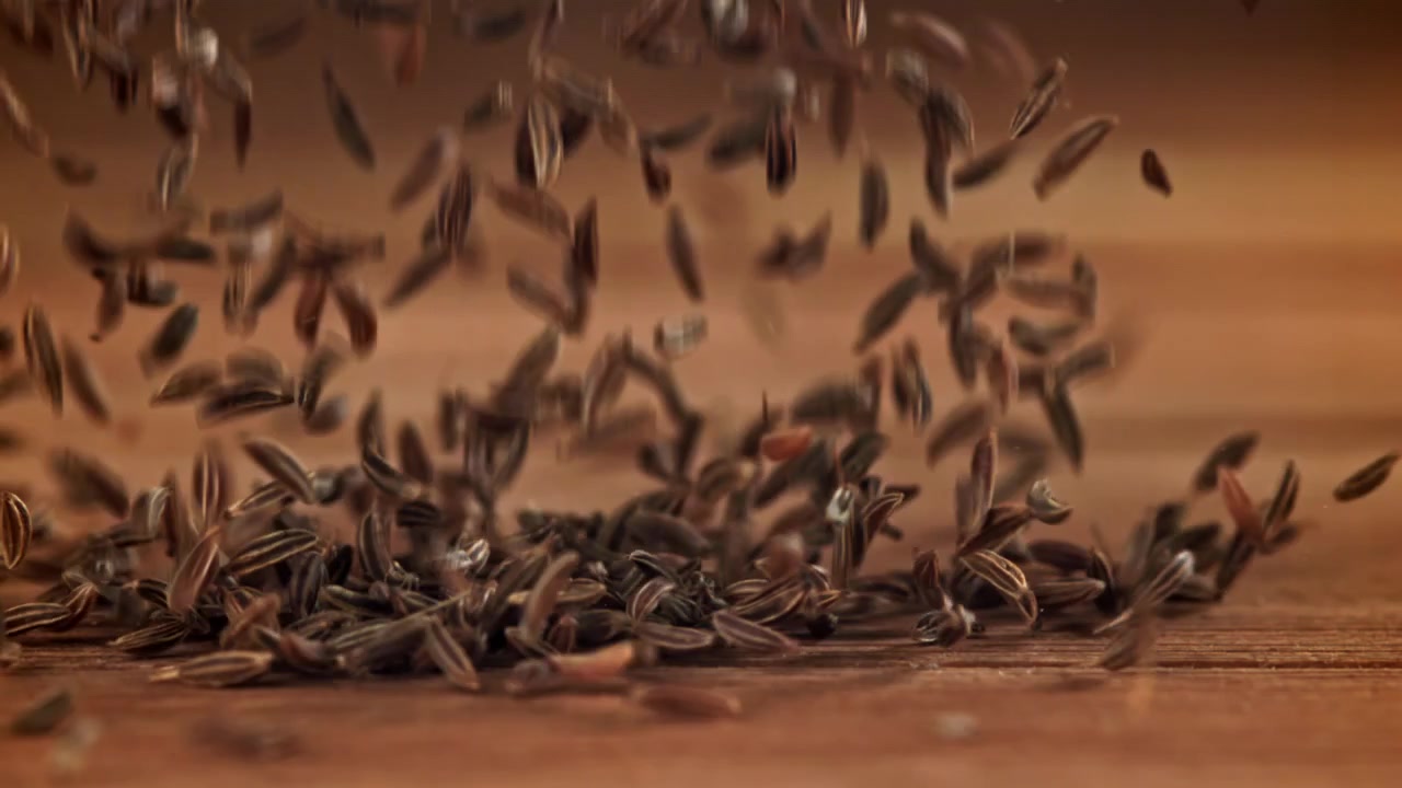 Cumin Seeds Falling onto a Wooden Surface in Slow Motion