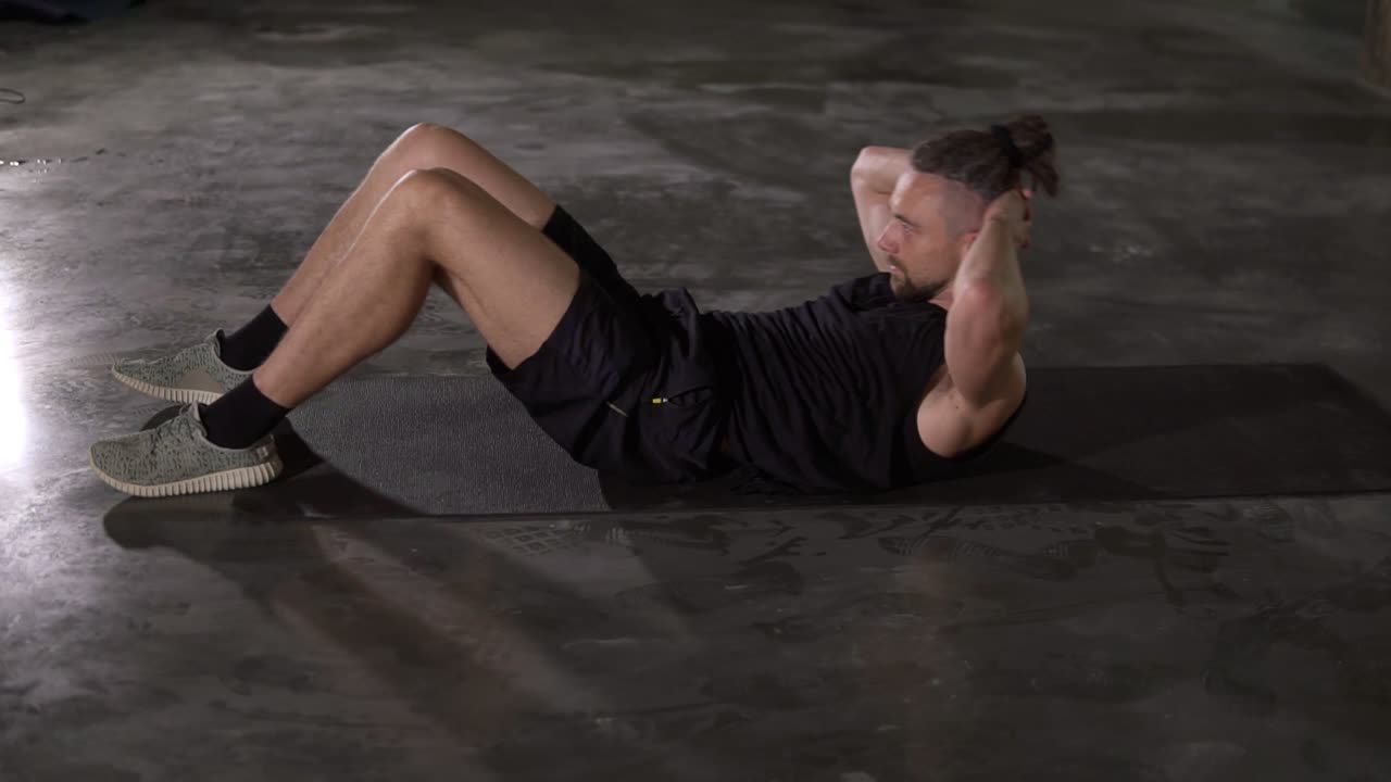 hombre musculoso en ropa deportiva haciendo ejercicio deportivo abdominal en un tapete de fitness usando solo en un estudio de loft. hombre haciendo ejercicios de fitness abdominal en cámara lenta