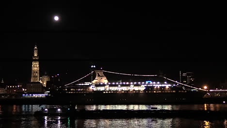 boat passing under a full moon at the antwerp skyline