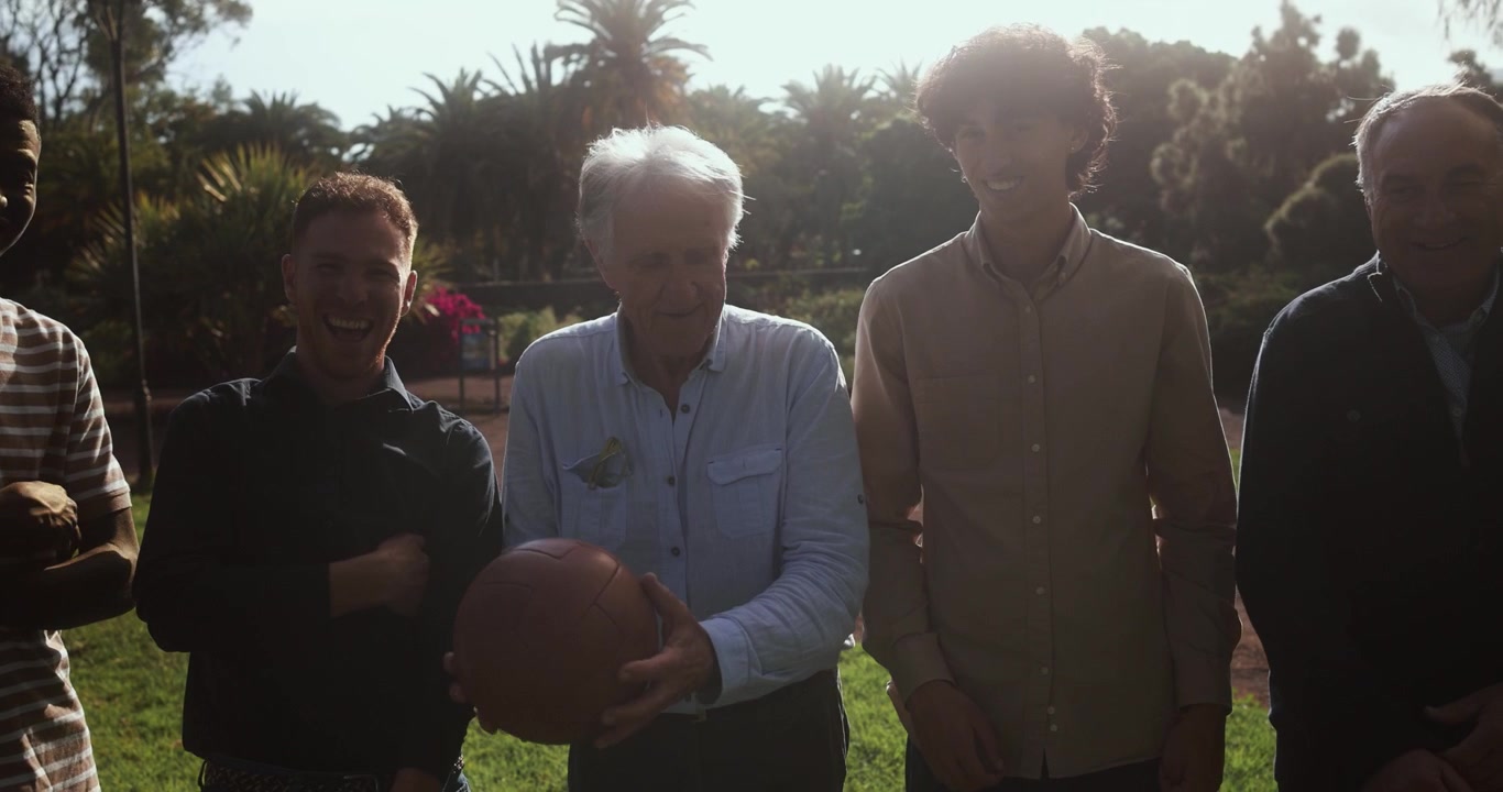 Uomini felici di diverse generazioni che giocano con un pallone d'epoca in un parco soleggiato