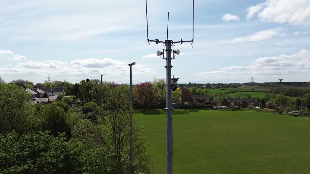 Aerial view rising over neighbourhood sports field to telecommunication tower for digital signals