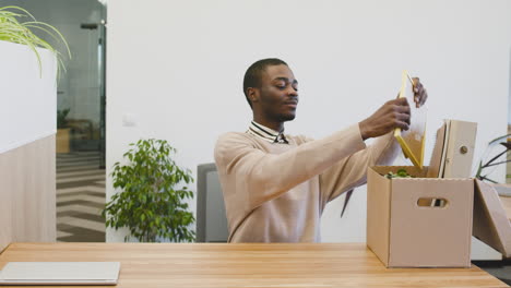 a young man places a box of his belongings on a table in his new office